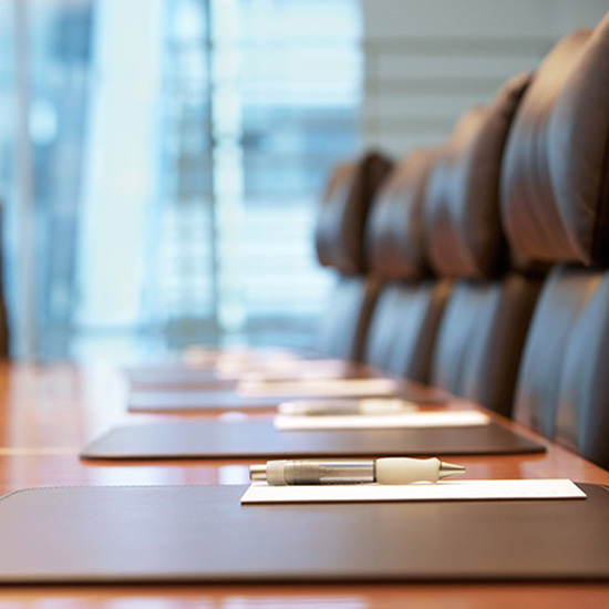 Board of Directors; Stylish boardroom with brown leather chairs, a polished wood table set with notepads and pens; a bright, professional atmosphere.