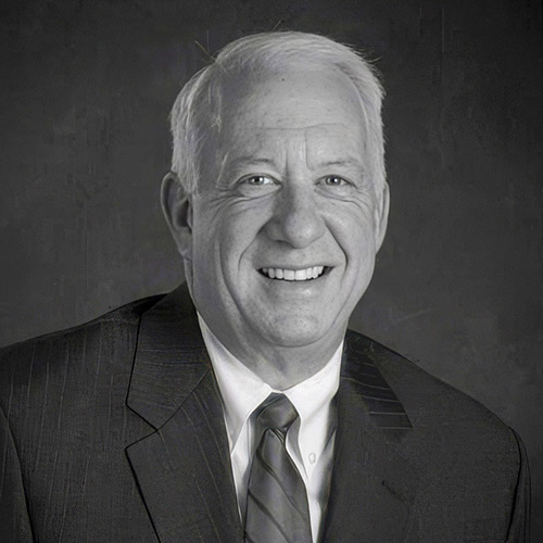 Byron Hansen; A black and white image of a man smiling in a suit and tie, conveying a professional tone.