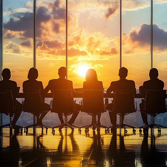 Insurance Trust Board of Directors; Silhouetted group of six people sitting at a conference table in front of large windows, with a vibrant sunset creating a warm, reflective ambiance.