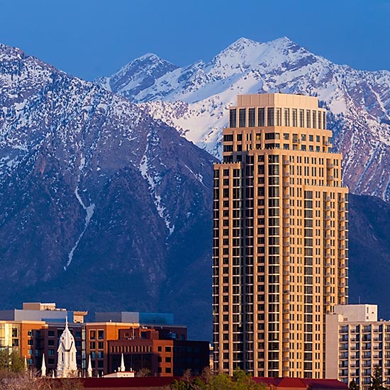 Recommended Vendors; A tall, modern skyscraper stands prominent against a backdrop of snow-capped mountains under a clear blue sky, conveying a sense of urban and natural beauty.